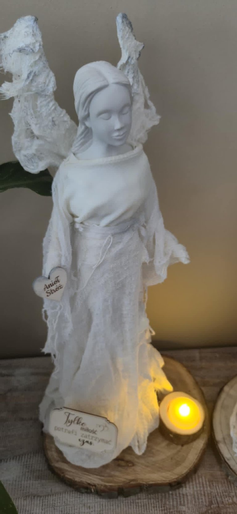 White statue of a woman with angel wings on a wooden base next to a glowing yellow LED candle