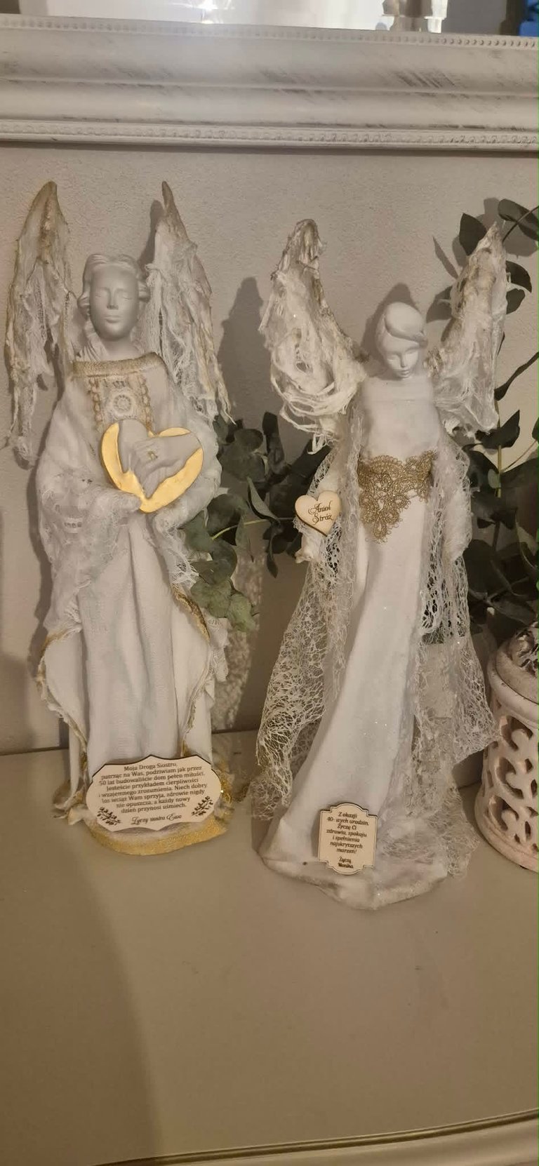 Three white ceramic angel figurines with delicate lace wings and gold heart-shaped plaques, displayed on a shelf