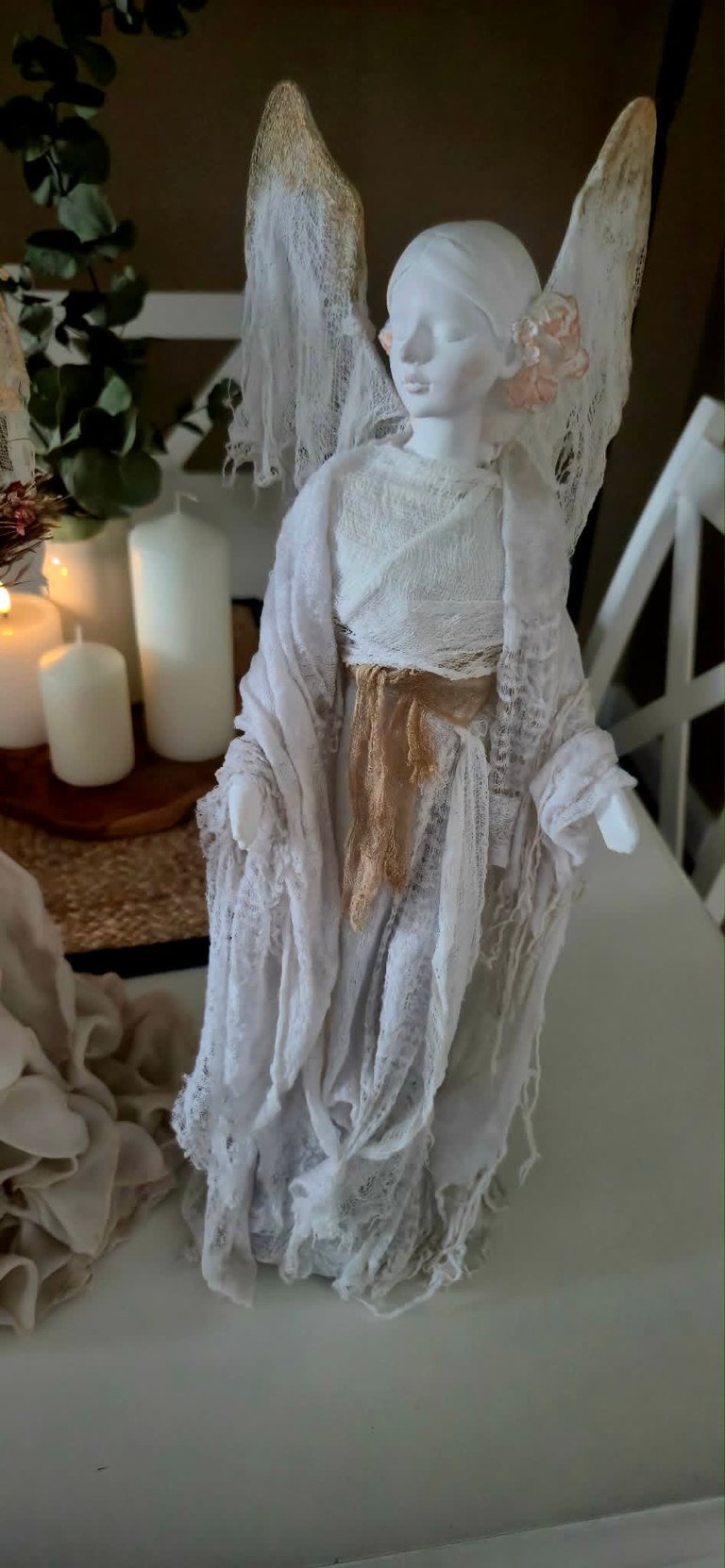 White lace angel figurine with wings and gold accents displayed on table with candles and greenery