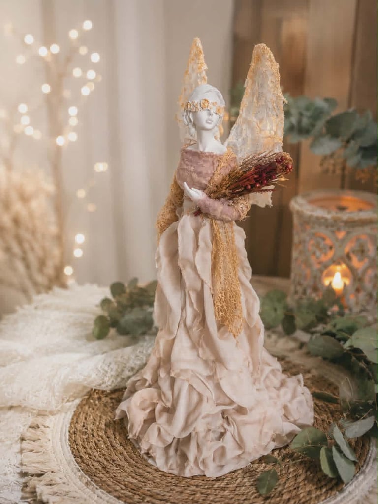 Decorative angel figurine with gold wings and cream dress holding a wreath, positioned on a rope coaster among holiday greenery and warm bokeh lights