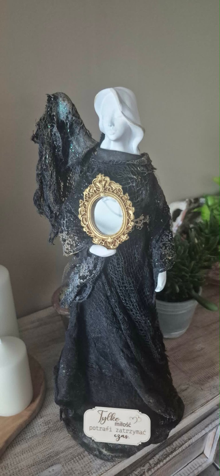 Gothic-style decorative figure with white mannequin head, black textured dress, gold oval cameo brooch, and fabric draping detail