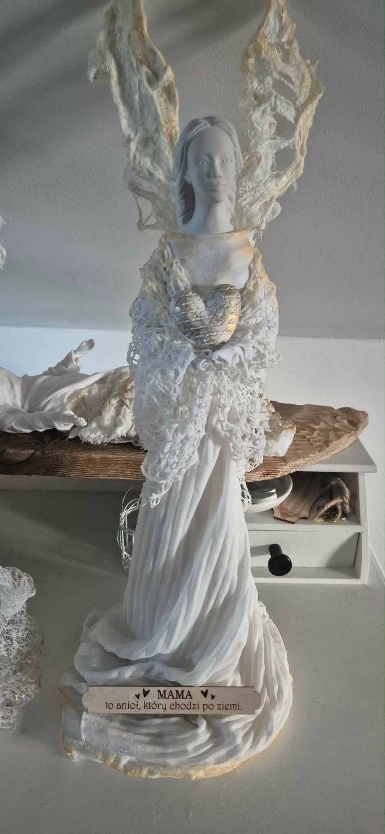 White porcelain angel figurine with lace wings and flowing gown, standing on wooden base with plaque, against white backdrop