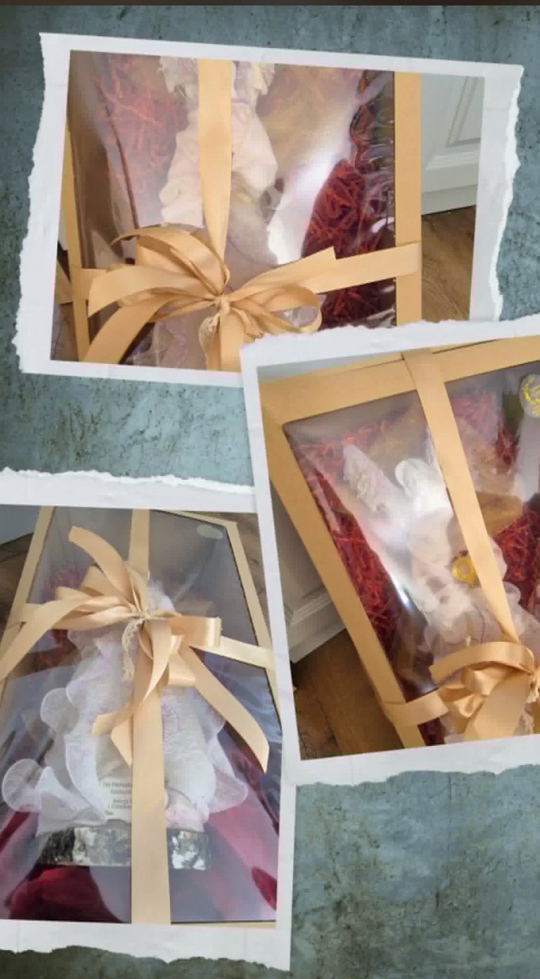 Three gift boxes with burgundy and pink fabric wrapped with white tissue paper and gold ribbons arranged on a blue textured surface