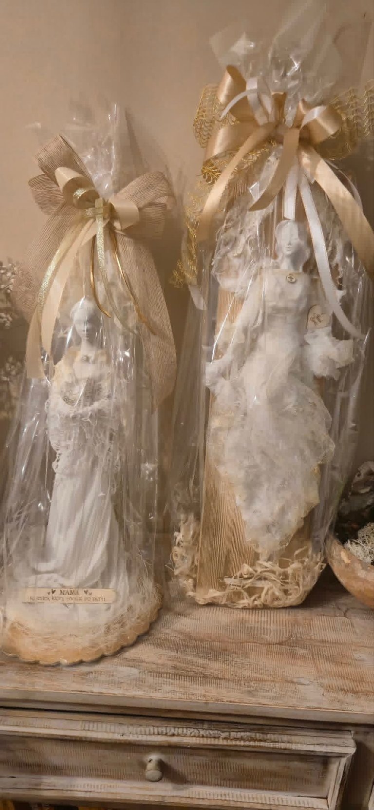 Two decorative bottles wrapped in clear cellophane with gold ribbon bows displayed on a wooden drawer