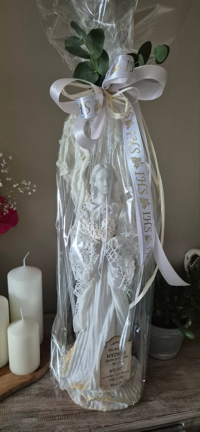 Wrapped bottle with white ribbon bow and green plant stems, displayed with candles and decorative items