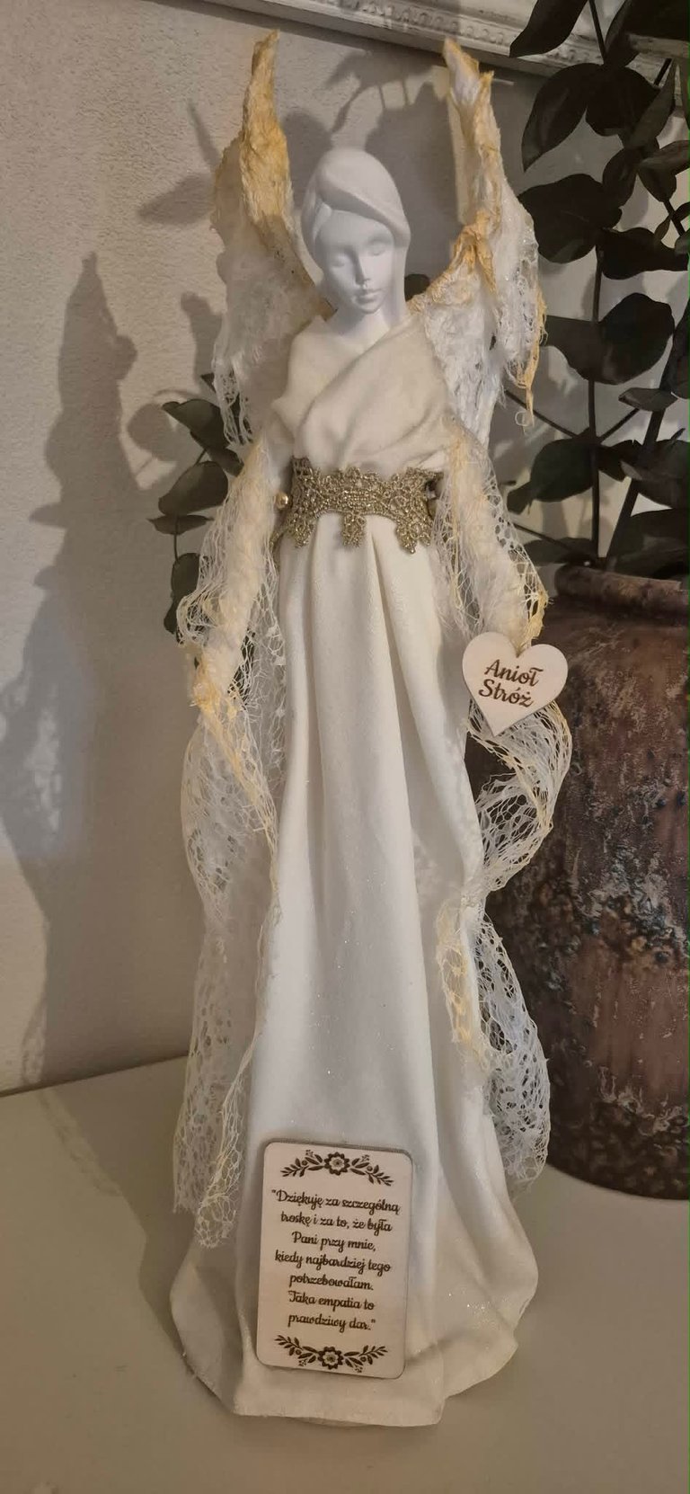 White porcelain angel figurine with lace wings and gold trim, wearing a gown and headpiece, displayed with decorative foliage