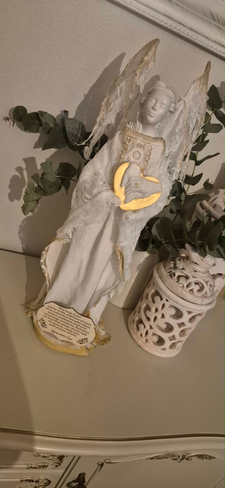 White angel figurine with gold accents and crescent moon, decorated with eucalyptus greenery and ornamental ceramic vase